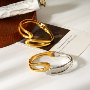 Detail of gold and silver two-tone U-shaped stainless steel bracelets on a wooden plate