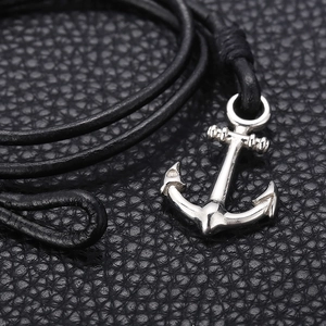 Macro detail of silver anchor pendant on black braided leather cord against textured background