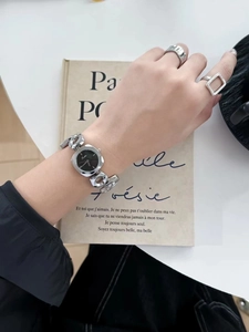 Elegant ladies' silver watch with a black square dial shown on a wrist with a book