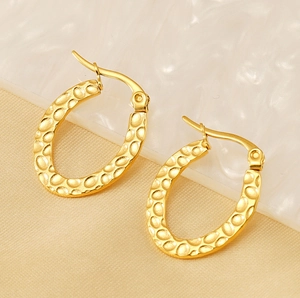 Detailed macro view of gold-plated oval earrings with hammered texture on white stone