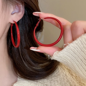 Detail view of large matte red round hoop earrings worn by a model in a retro style