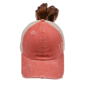 Close-up of coral pink distressed mesh trucker hat with integrated brown ponytail