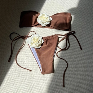 Detail of chocolate brown bikini set featuring large 3D white rose accents and side ties