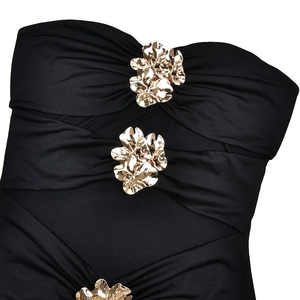 Detalle de vestido negro sin hombros con flores de metal dorado y textura de tela plisada