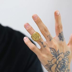 Detail of a gold embossed coin ring with religious cross design on a male hand