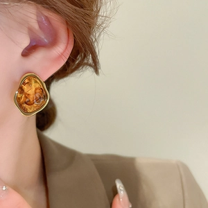 Detail of an irregular geometric amber resin earring with gold metal trim on model