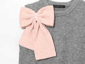 Dettaglio del gilet in maglia grigia con grande fiocco rosa e trama di lana morbida