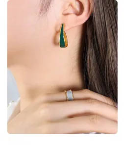 Detail of green enamel U-shaped earrings and grey ring on model with golden metal trim