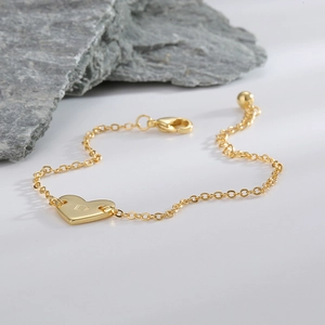 Bracelet cœur doré minimaliste avec un pendentif gravé de la lettre D sur fond blanc