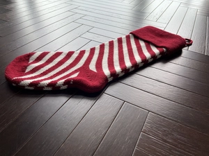 Close-up of red and white striped knitted Christmas stocking on wooden background