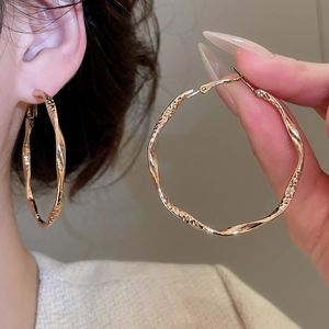 Detailed view of large gold textured hoop earrings with irregular hammered finish on model