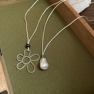 Detailed view of silver wire flower pendant and baroque pearl on beige cord necklaces