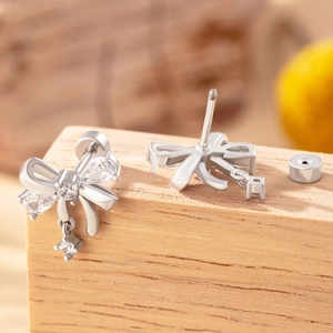 Silver bow stud earrings with sparkling zircon crystals and screw back on wood surface