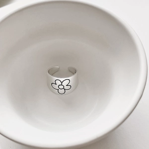 Detailed view of adjustable silver flower ring with black floral motif in a ceramic bowl