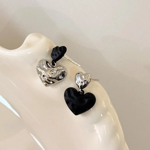 Asymmetric liquid metal heart stud earrings in silver and black on a ceramic tray
