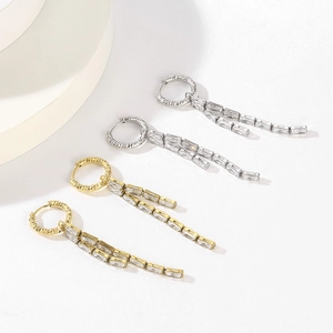 Close-up of gold and silver tassel earrings with rectangular zircons and wavy rings
