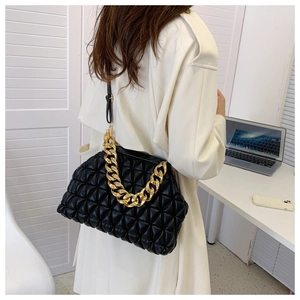 Detail of black quilted shell bag with gold chain and leather strap on white coat