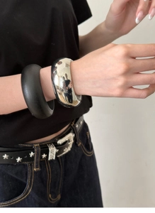 Close-up of minimalist glossy silver and matte black thick bangles worn by a model