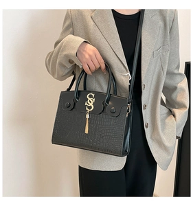 Detail view of black crocodile pattern crossbody bag with gold logo and tassel accent