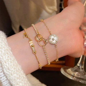 Detail of layered gold bracelets featuring clover charm and cubic zirconia link design