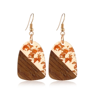 Macro detail of geometric drop earrings with dark wood and gold leaf resin textures