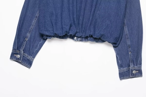 Detailed view of denim jacket featuring elastic waistband and metal snap button cuffs