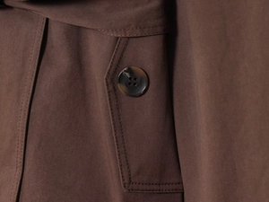 Detailed close-up of dark brown trench coat fabric texture, stitching, and amber button