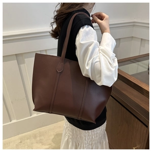 Detail of leaf-shaped handle reinforcement and vertical stitching on brown leather tote bag