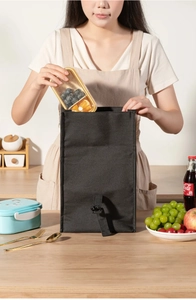 Black insulated lunch bag with buckle closure showing clear bento box with fresh fruit