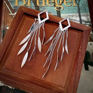 Detailed view of silver leaf sequin tassel earrings on a vintage wooden jewelry tray