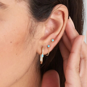 Detailed view of turquoise stud earrings and gold hoop earring worn by a model