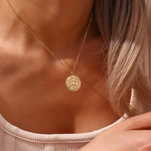 Dettaglio di una collana con ciondolo a moneta d'oro con texture e zircone su una modella