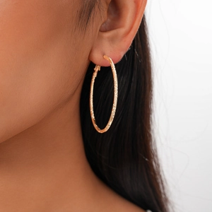 Detailed close-up of a gold textured hoop earring worn by a model on a white background