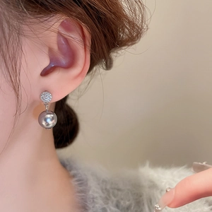 Close-up of silver stud earring with cubic zirconia and hanging grey pearl on model