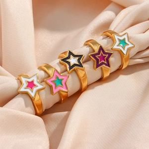 Five gold rings with colorful star enamel charms on elegant beige silk fabric