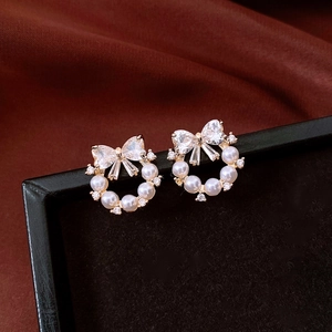 Detail view of gold bow knot earrings with pearls and cubic zirconia on a silk background