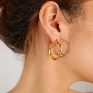 Close-up of elegant gold twisted hoop earrings worn by a model showcasing texture