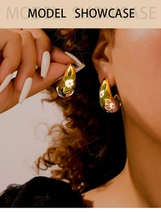 Detailed close-up of C-shaped gold-plated enamel earrings with floral leaf patterns