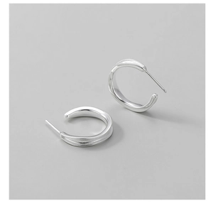Close-up of polished S925 sterling silver C-shaped hoop earrings on gray background