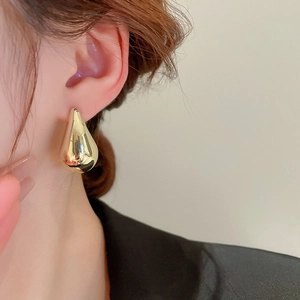 Detail of large polished gold teardrop earring on model with glossy mirror finish