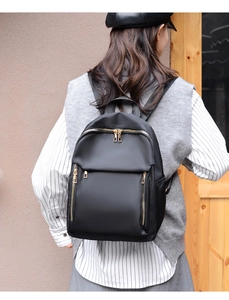 Rear view of model wearing black nylon backpack with golden zippers and multi-pockets