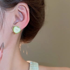 Macro shot of cute green apple slice earrings with small smile on a female ear