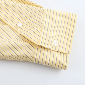 Close-up of long sleeve cuff with white buttons on yellow striped shirt fabric