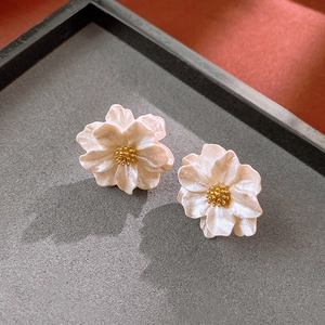 Macro shot of French style cream flower earrings with golden center on gray velvet