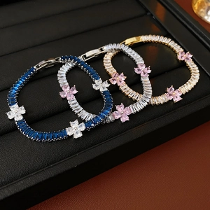 Detailed shot of sparkling zircon clover bracelets in silver and gold on a leather tray