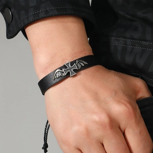 Close-up of black braided leather bracelet featuring vintage silver cross and wing charm