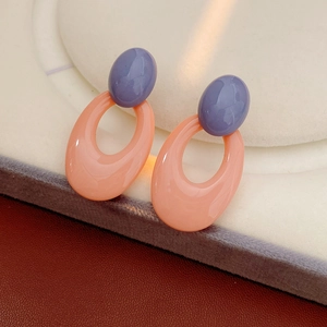 Detail of pink-orange oval hoop earrings with purple resin beads on a textured surface