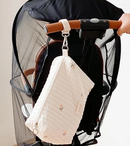 Close-up of quilted cream baby stroller bag with tulip embroidery hanging on handle