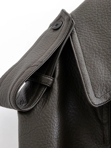Détail de la texture similicuir marron foncé avec coutures d'épaule et boutons noirs