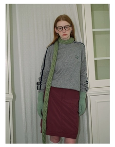 Detail of a green chunky knit scarf paired with a grey sweatshirt and burgundy skirt